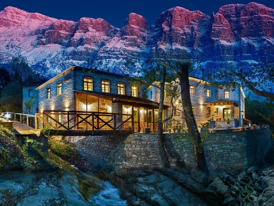 Traditional stone guesthouse in Papigo village, Zagorochoria, Epirus, with snowy mountains in the background during winter